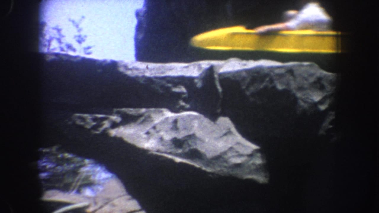 Yellow ride vehicle moving past artificial rocks near a bright opening.
