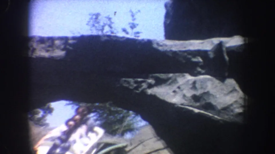 A white ride vehicle with visible riders appears below artificial rockwork in the 1962 Anaheim park footage.
