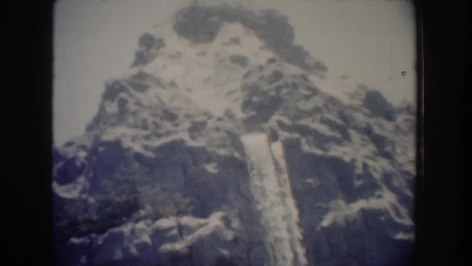 1962 Anaheim home-movie view of a vertical waterfall cutting through a rugged rock face under a pale sky.
