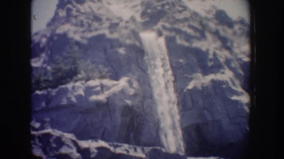 Faded 1962 Anaheim 8mm frame showing the waterfall lower on the rocky mountain face, with ledges and white edging around it.