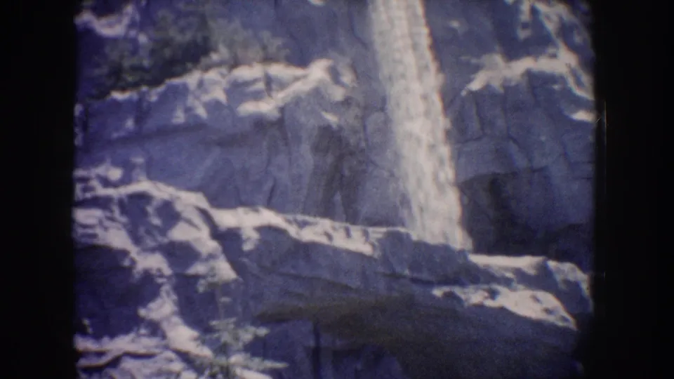 1962 Anaheim 8mm home-movie frame with the waterfall centered beside dark rock ledges and a prominent foreground ridge.