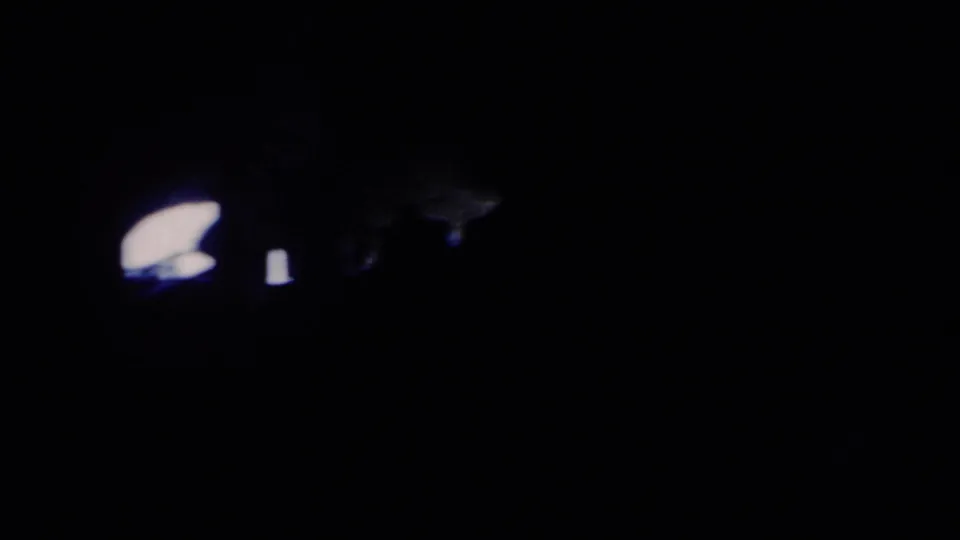 Dim 8mm frame from the Anaheim clip with only small bright highlights and faint surrounding rock forms visible.