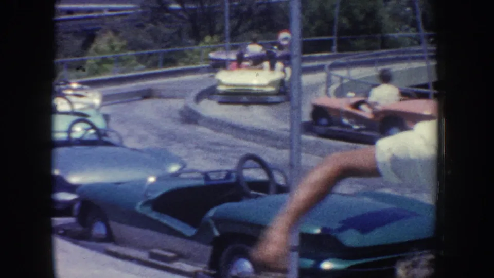 1962 Anaheim ride scene with teal, yellow, and red bumper cars moving around an outdoor amusement-park track.