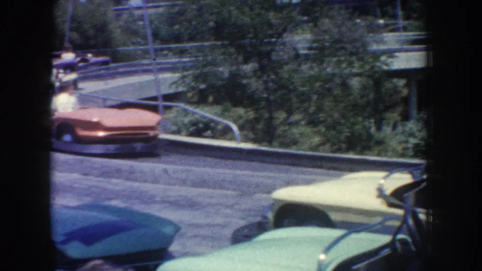 1962 Anaheim home-movie frame showing colorful bumper cars beside railings, trees, and a curved amusement-park route.