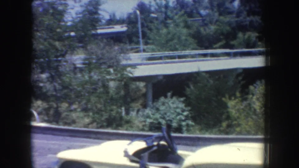 1962 Anaheim amusement-park frame with a yellow bumper car at the lower edge and landscaped ride surroundings behind it.