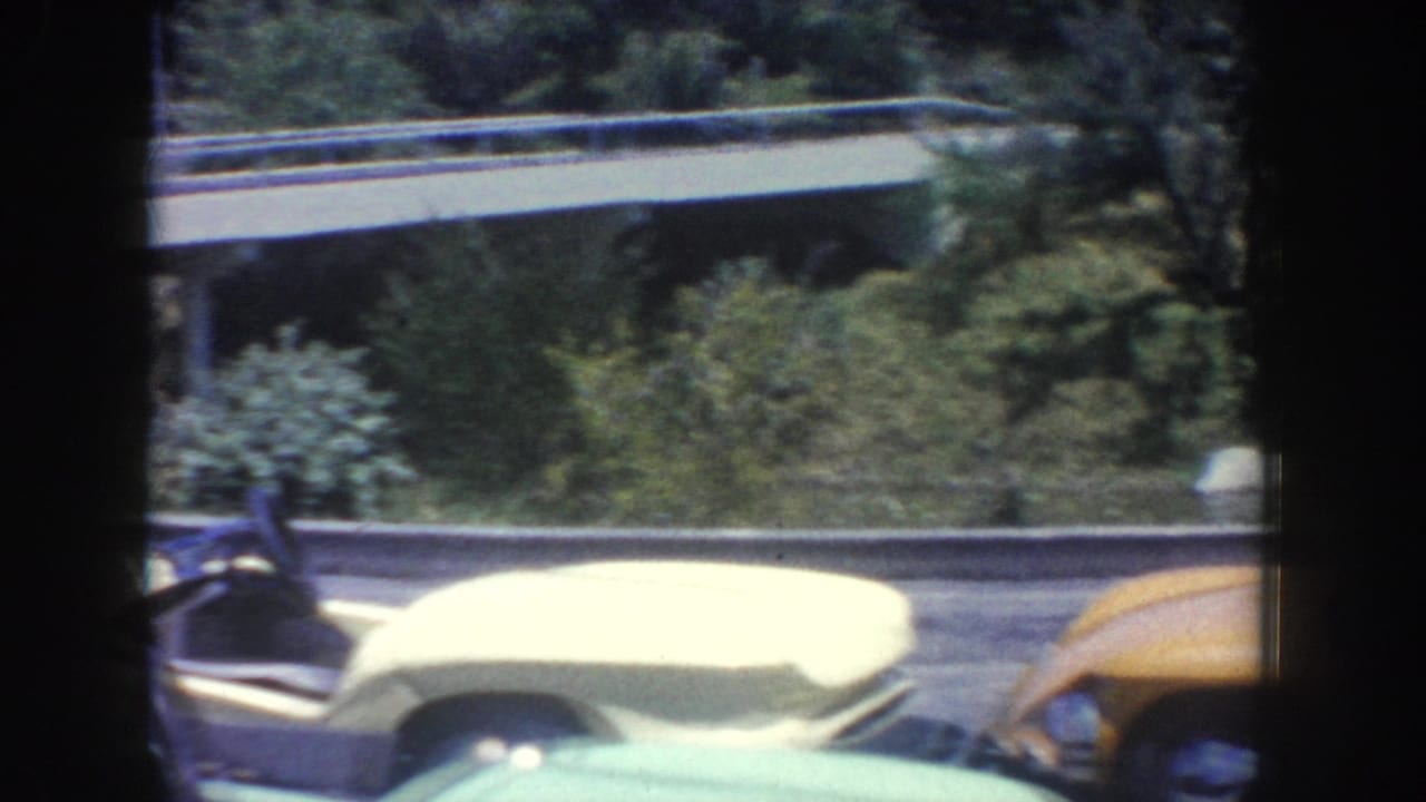 1962 Anaheim-area home-movie frame showing classic cars, including a pale yellow convertible, beside a tree-lined road and overpass.