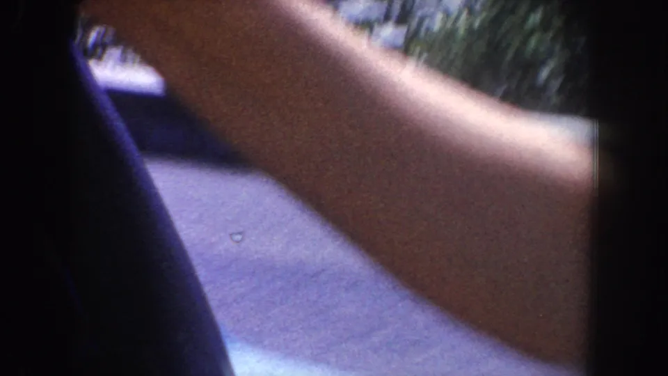 Passenger-side 8mm view inside a moving car, with a person's arm in the foreground and blurred road surface outside.