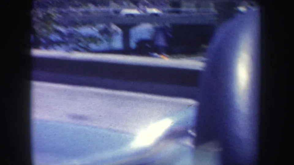 Close partial view of a person near the car window during the 1962 Anaheim-area drive, with guardrail and road visible outside.