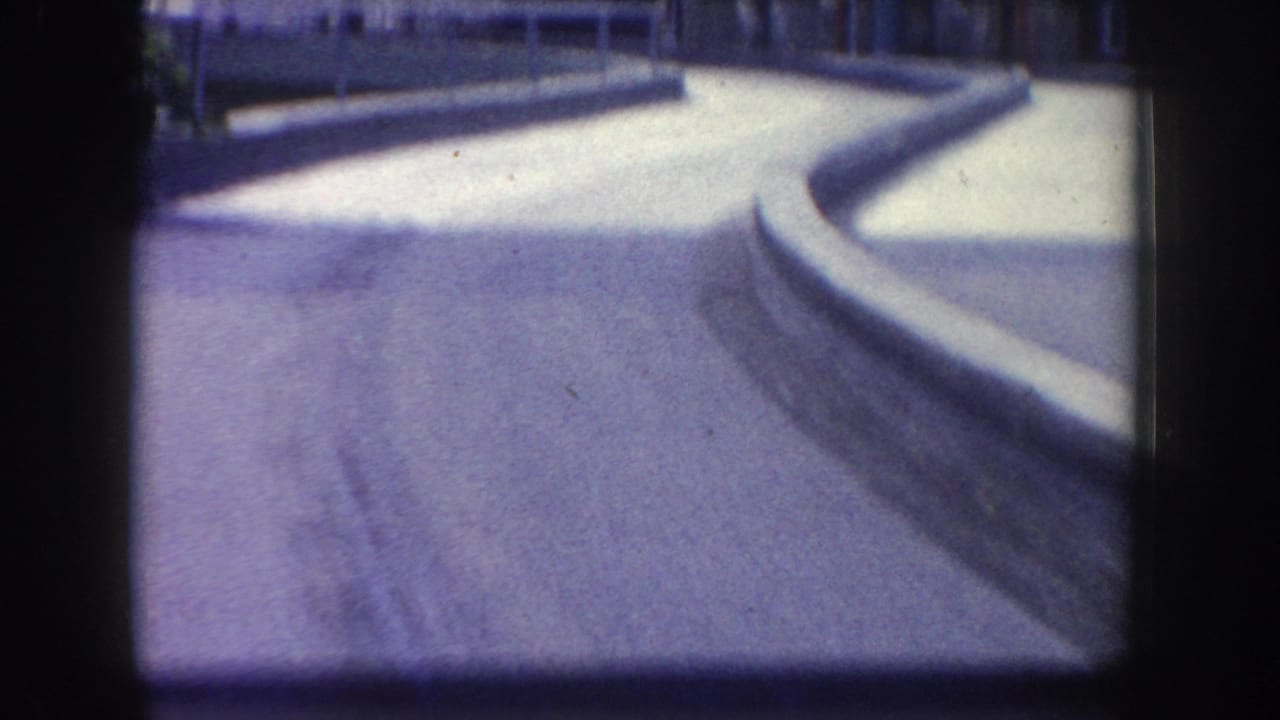 Soft-focus 1960s Anaheim home-movie frame showing a curved paved walkway, raised curb, and dark film gate edges.