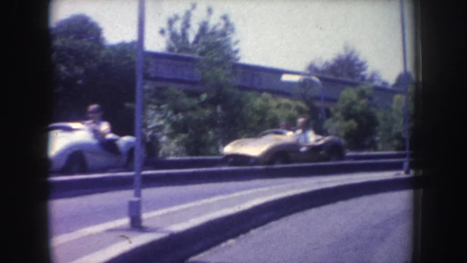1962 Anaheim frame showing a silver open-top classic car with visible occupants on a road below an elevated structure and streetlights.