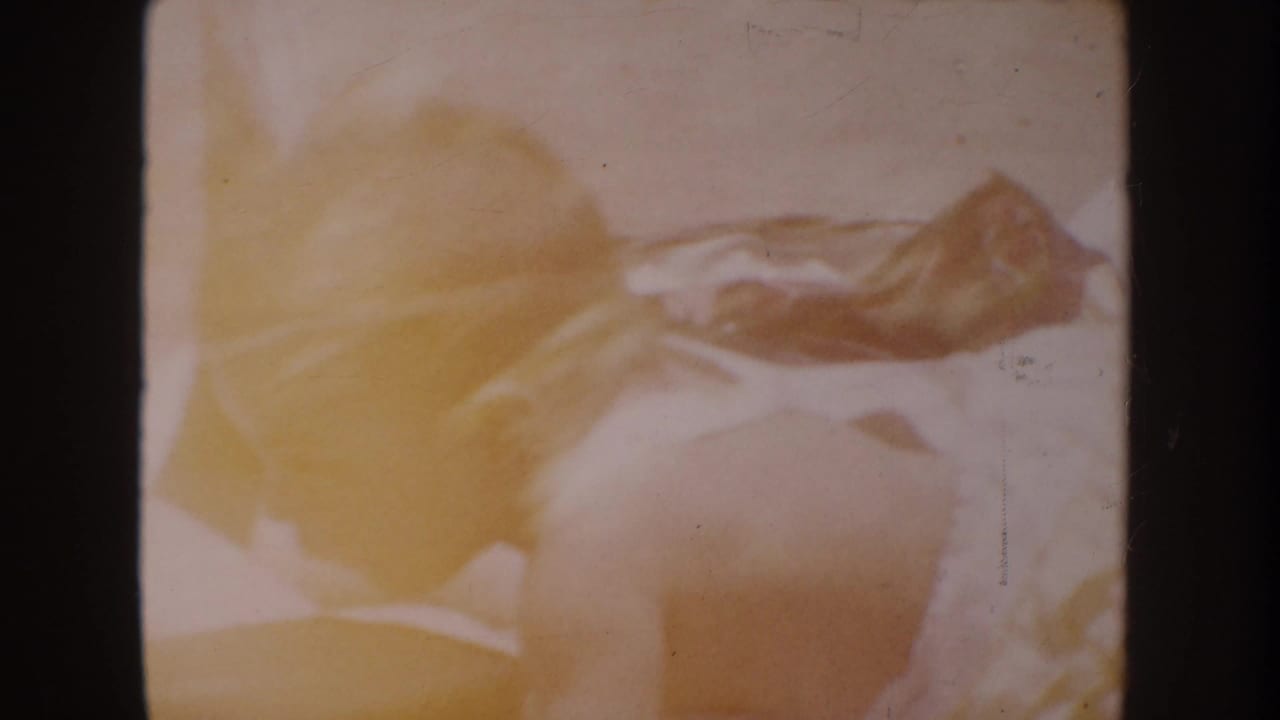 Partially visible baby lying on pale bedding within a dark 8mm film frame.