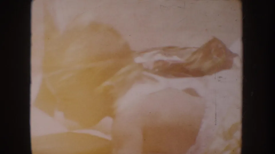 1962 Anaheim home-movie frame showing a partially visible baby on pale bedding, softened by faded color and film wear.
