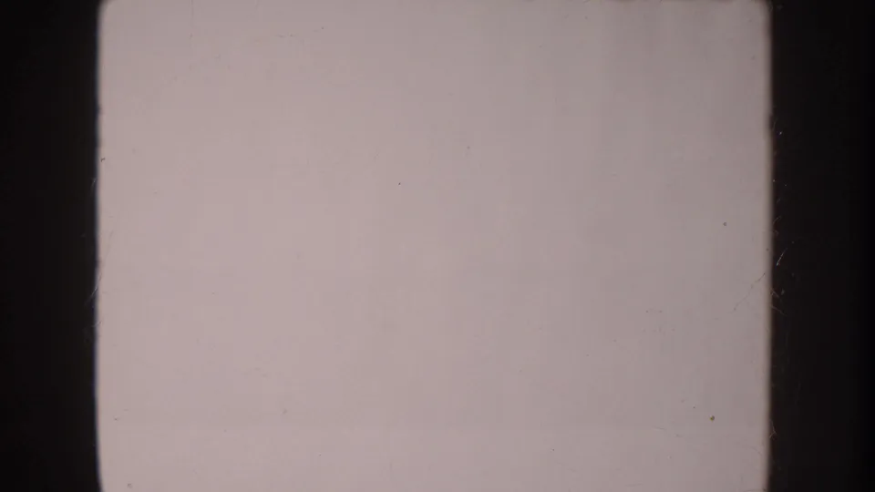 Pale blank 8mm frame with visible grain, scratches, and dark frame edges from the Anaheim home-movie clip.