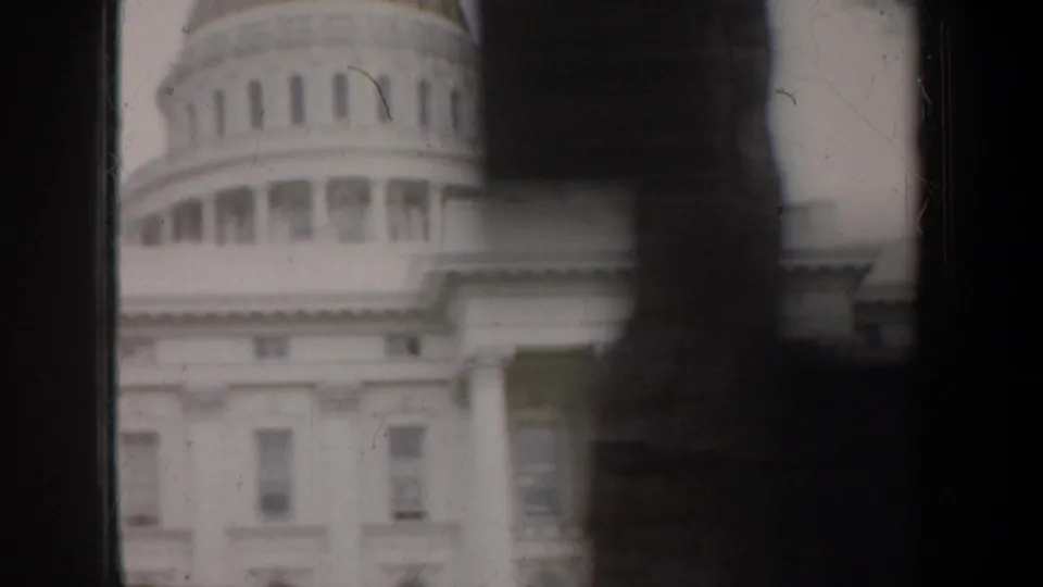1957 8mm travel frame showing a domed white civic building partly obscured by the passing vehicle's dark window frame.