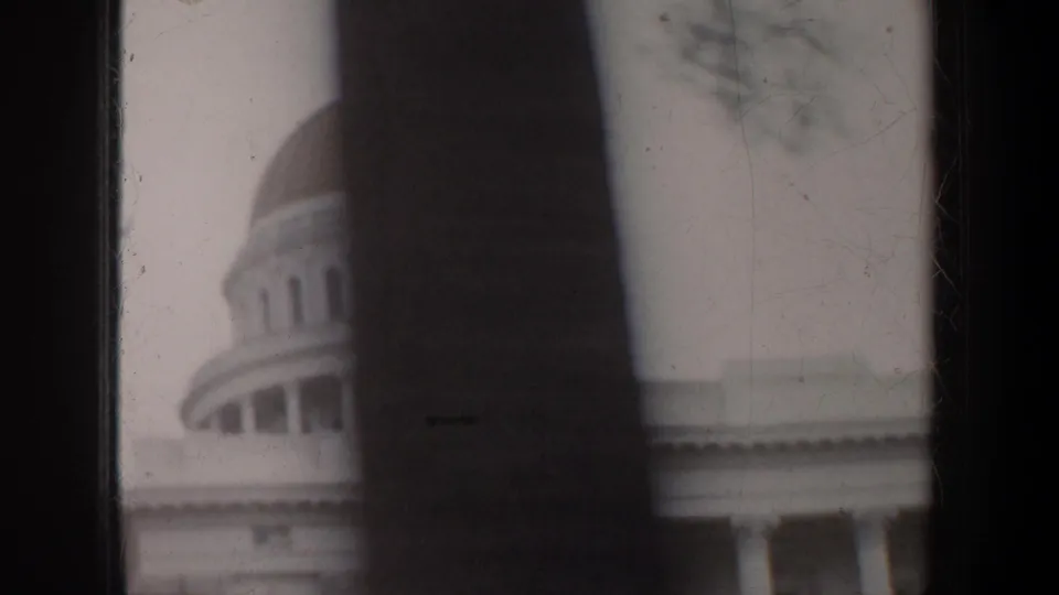 1950s 8mm frame of the California State Capitol dome seen through trees, with soft focus and visible film wear.
