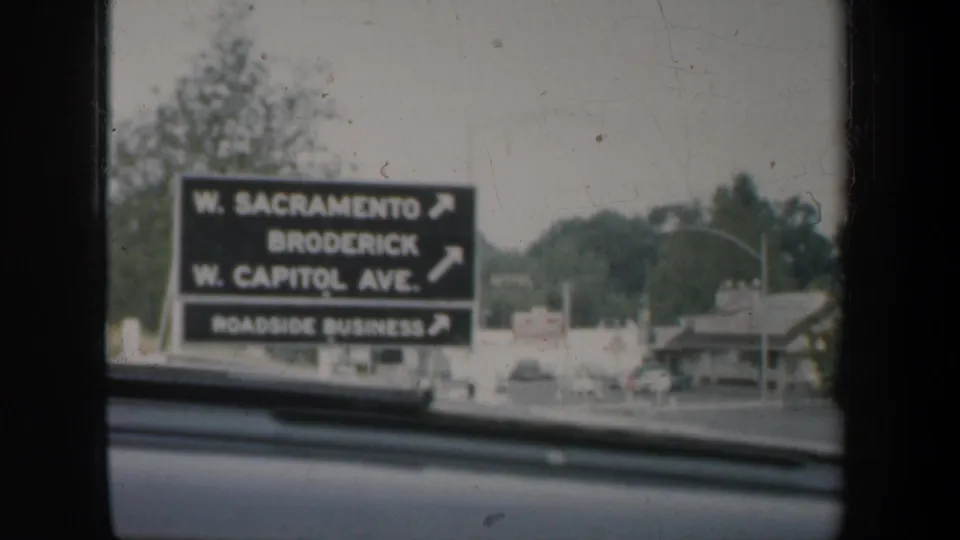A roadside directional sign for W. Sacramento, Broderick, and W. Capitol Ave. is seen through a car windshield.