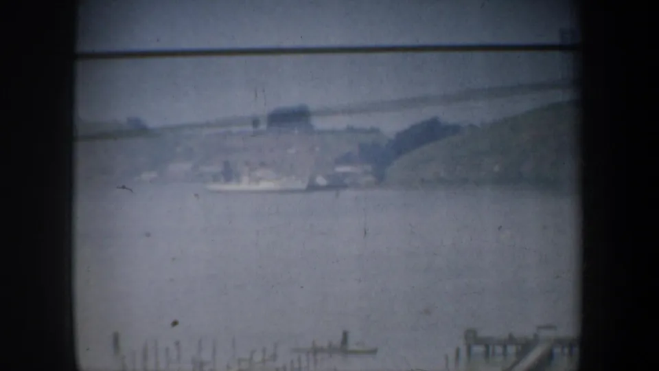 1957 home-movie frame looking across water toward a low hillside and small shoreline features in the San Francisco area.