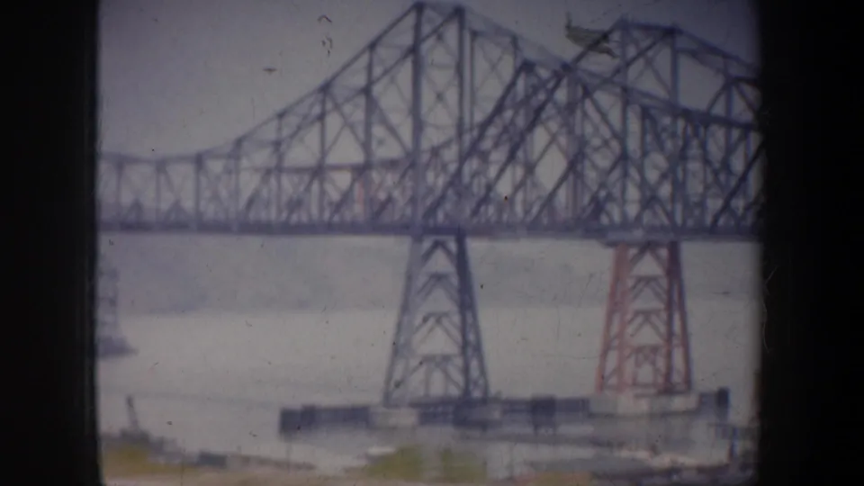 Large steel truss bridge over water in the San Francisco area, filmed softly from a moving vehicle in 1957.