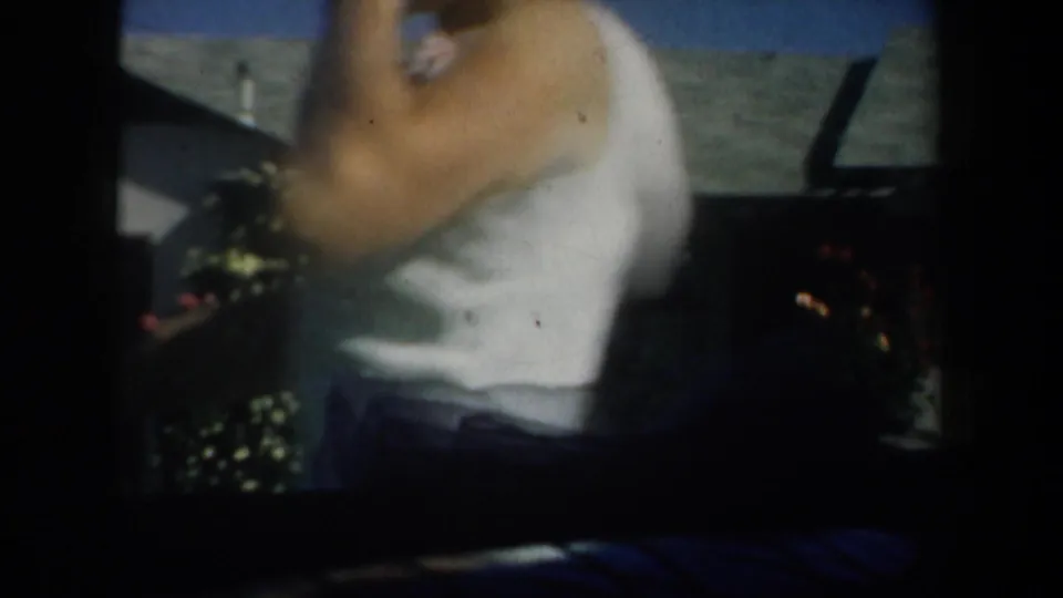 1957 San Francisco-area home-movie frame with a blurred partial adult figure beside a patio or yard overlooking water.
