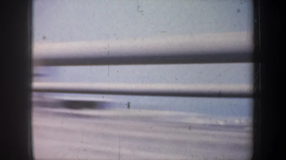 Bridge railings sweep across a soft 1957 San Francisco bay view from inside a moving vehicle, with water and sky beyond.