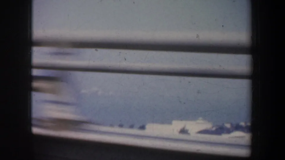 1957 car-window view across bridge rails toward bay water and a low distant shoreline, framed by the dark vehicle interior.