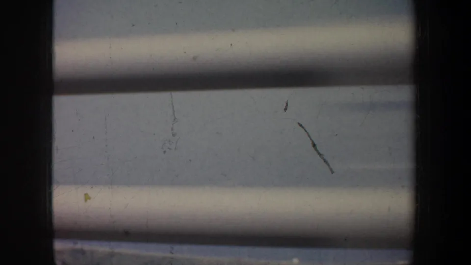 A stationary 1957 home-movie view through blinds, with faint exterior detail and visible film scratches.