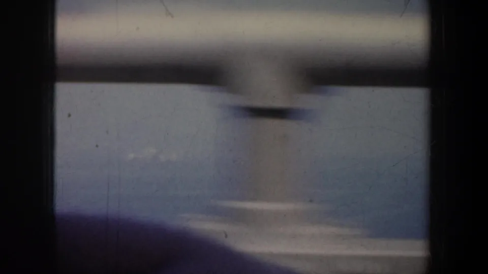 Soft 8mm frame from San Francisco showing blinds, a blurred foreground shape, and a hazy exterior beyond.