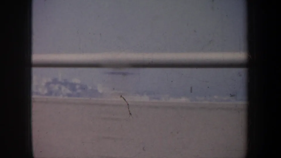 Final 1957 San Francisco bridge-crossing frame with dark supports, railings, water, and a faint shoreline beyond.