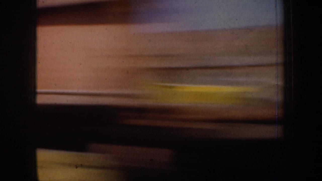 1957 8mm travel footage frame showing a blurred snowy mountain view through dark vehicle window divisions.