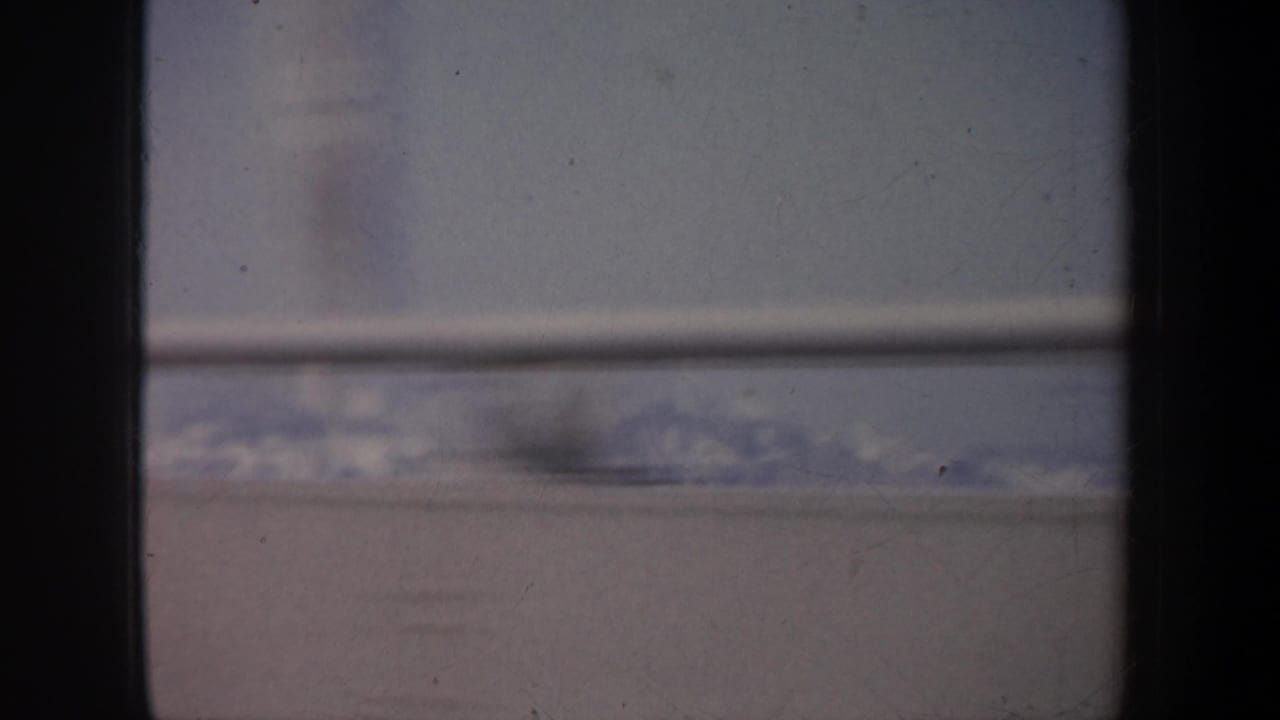 Faded 8mm frame of snow-covered mountains and pale sky seen through a vehicle window in the metadata-listed California setting.