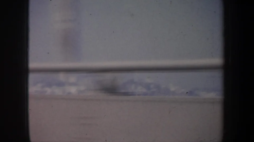 Faded 8mm frame of snow-covered mountains and pale sky seen through a vehicle window in the metadata-listed California setting.