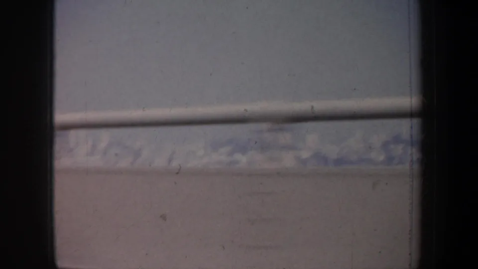 1957 home-movie frame with a low snowy ridgeline, horizontal window bar, and dark vehicle framing across the view.