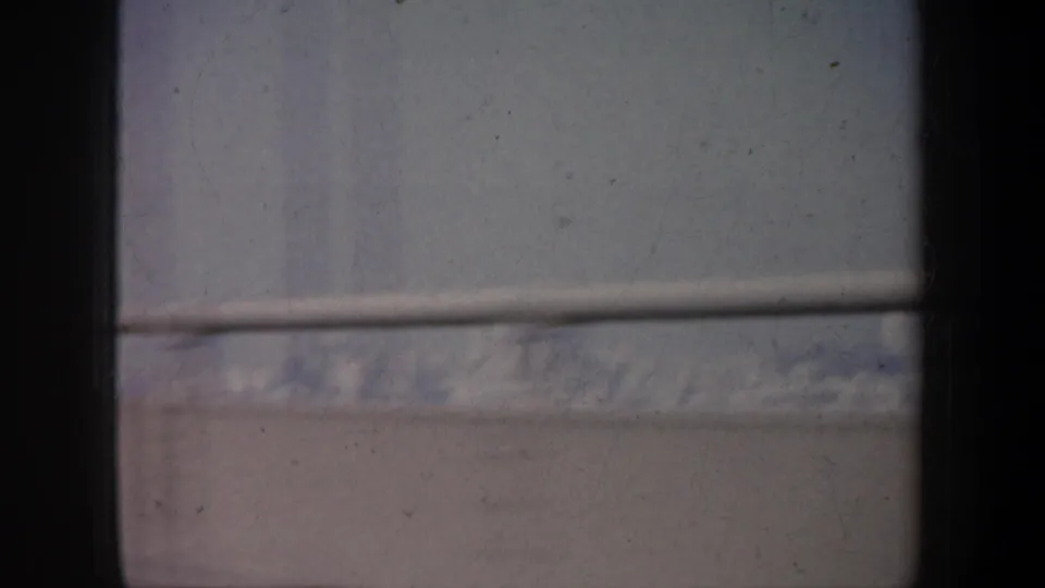 Faded 8mm frame of a distant snow-covered ridgeline viewed through dark vehicle window framing.