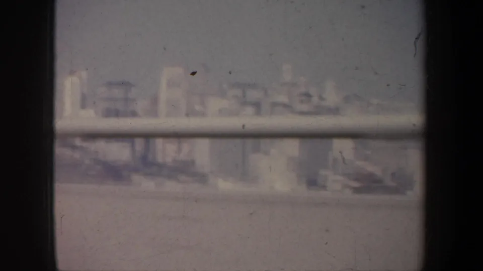 1957 San Francisco skyline or waterfront buildings appear in soft focus through a vehicle or transit window.
