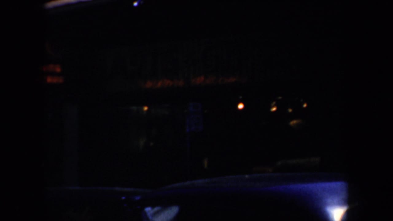Very dark street view with storefront reflections and part of a vintage car.