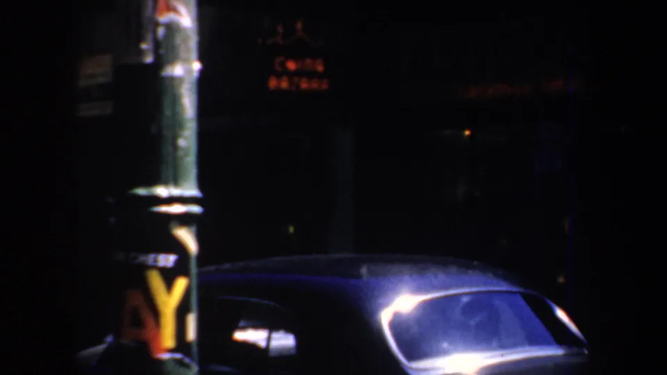 Nighttime San Francisco street view with a marked pole and dark mid-century car in low light.
