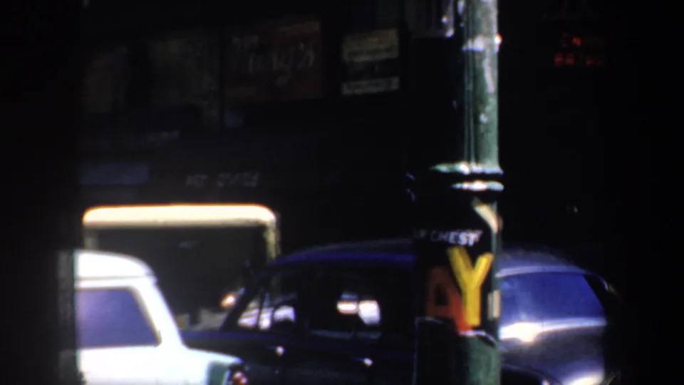 1957 San Francisco nighttime street frame showing vintage cars, a white vehicle, and faded pole advertising.