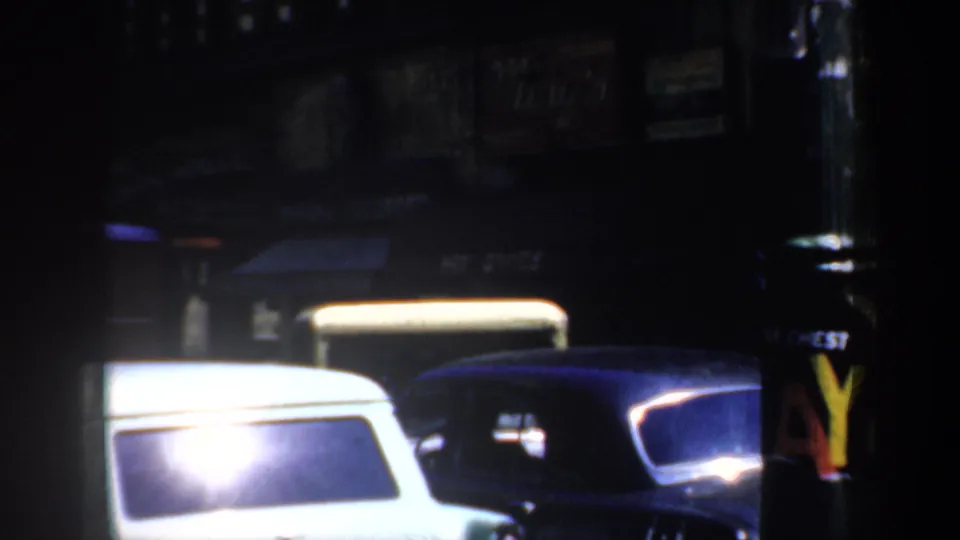 1957 San Francisco street at night with parked mid-century cars, storefront awnings, and bright reflections in the film frame.