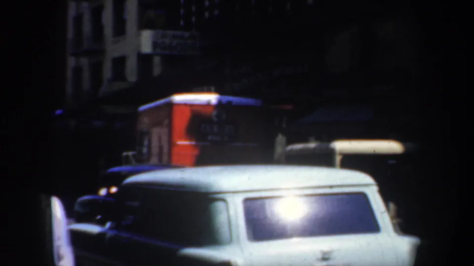 1957 San Francisco street frame showing parked mid-century cars beneath awnings and signage in low nighttime exposure.
