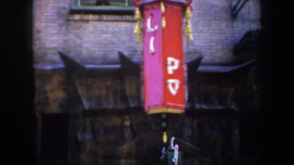 Close street detail of a vertical red and pink sign with Chinese characters on a brick facade in San Francisco.