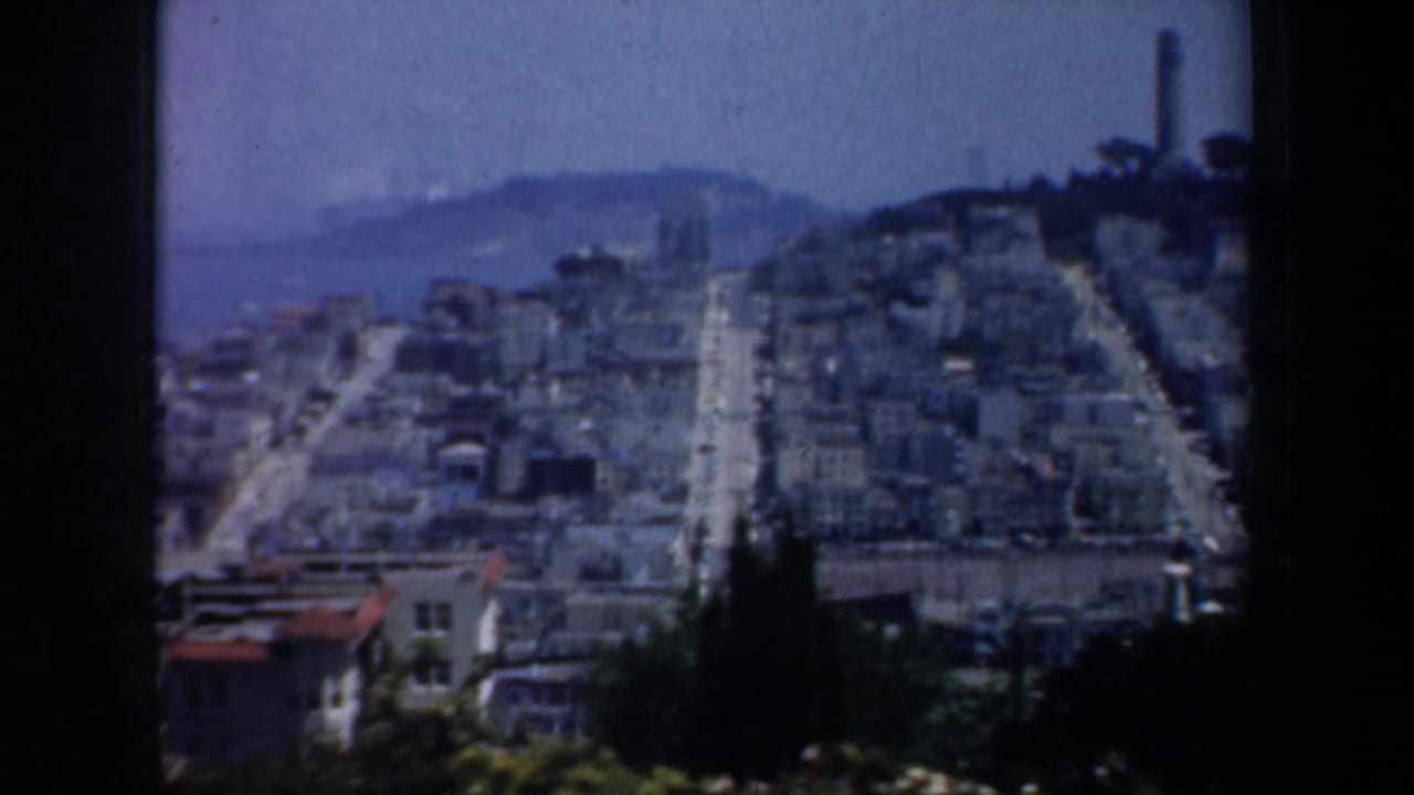 Elevated view over steep San Francisco streets with dense buildings and a distant tower.