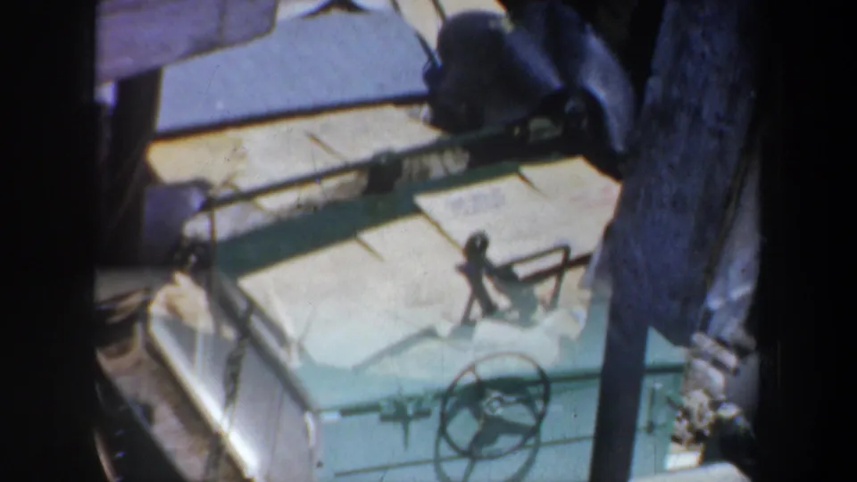 1957 San Francisco home-movie frame showing a green boat deck, steering wheel, rope, and a vertical piling or tree trunk in soft exposure.