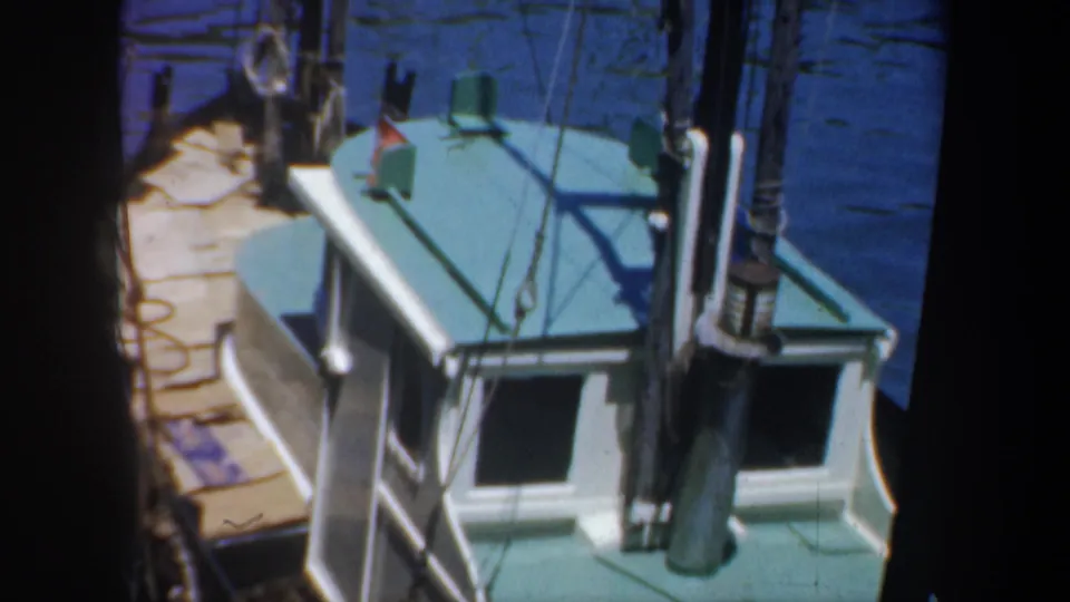 1957 San Francisco home-movie frame showing a small boat cabin with green roof, rigging, ropes, and dockside wooden planks.