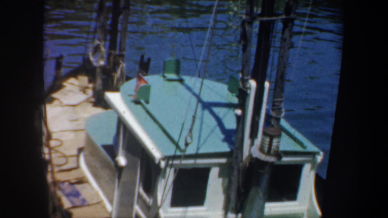 Teal-and-white boat cabin beside a wooden pier with rigging over calm water.