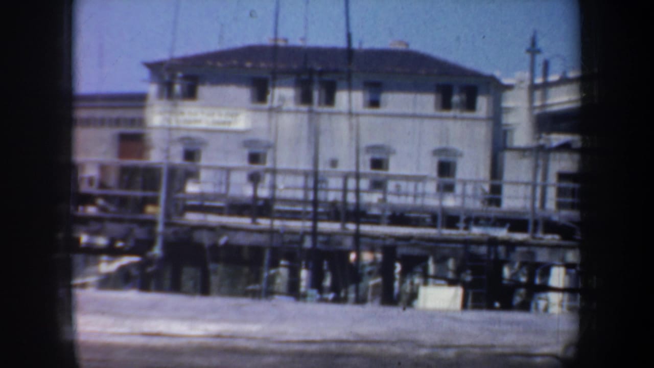 1957 San Francisco waterfront frame with a white port building, pier railings, and dark film-gate borders.