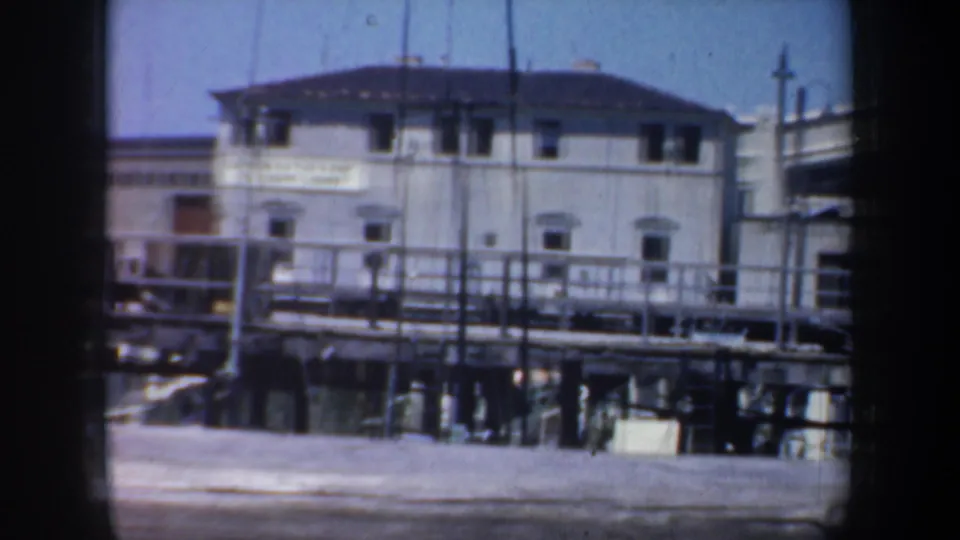 1957 San Francisco waterfront frame with a white port building, pier railings, and dark film-gate borders.