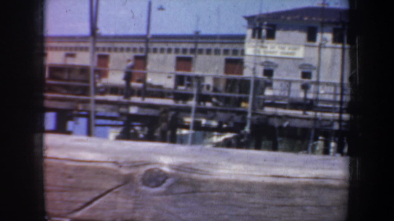 Port building and dock railings viewed across a horizontal wooden foreground.