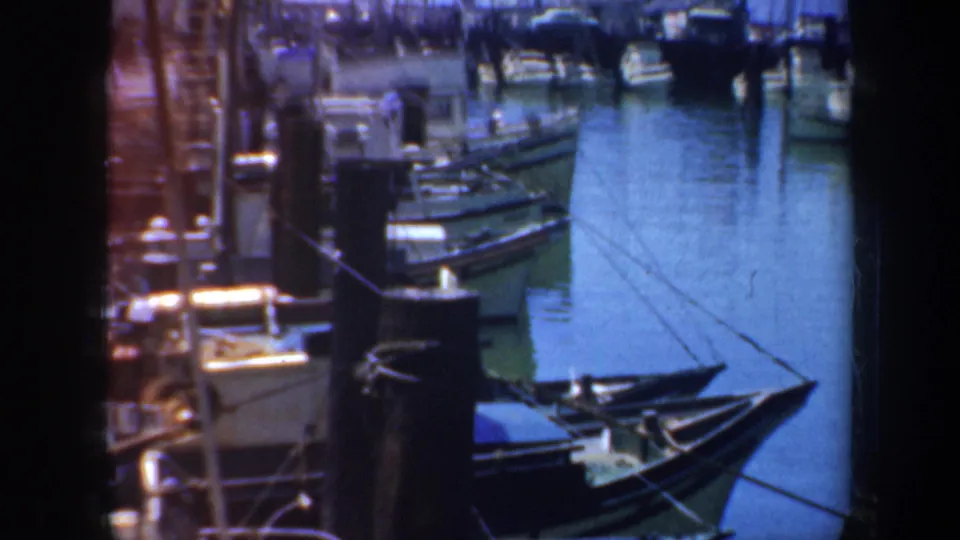 1957 San Francisco harbor footage showing small boats tied near a wharf, blue water, ropes, and dock structures in a soft 8mm frame.