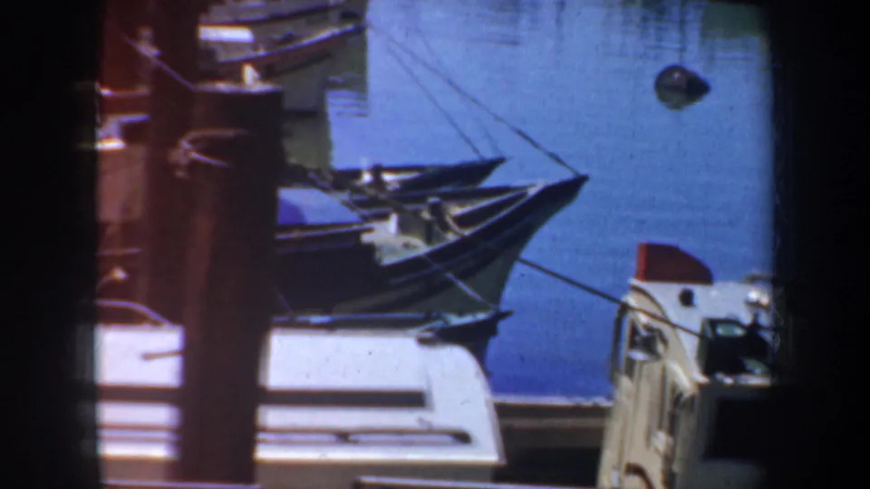 1957 San Francisco waterfront view with small boat bows, mooring lines, dock structures, and calm blue water captured on 8mm film.
