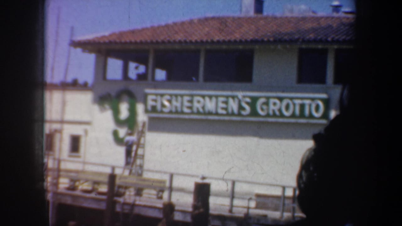 Fishermen's Grotto exterior sign beside a dock, with a ladder and worker near the building.